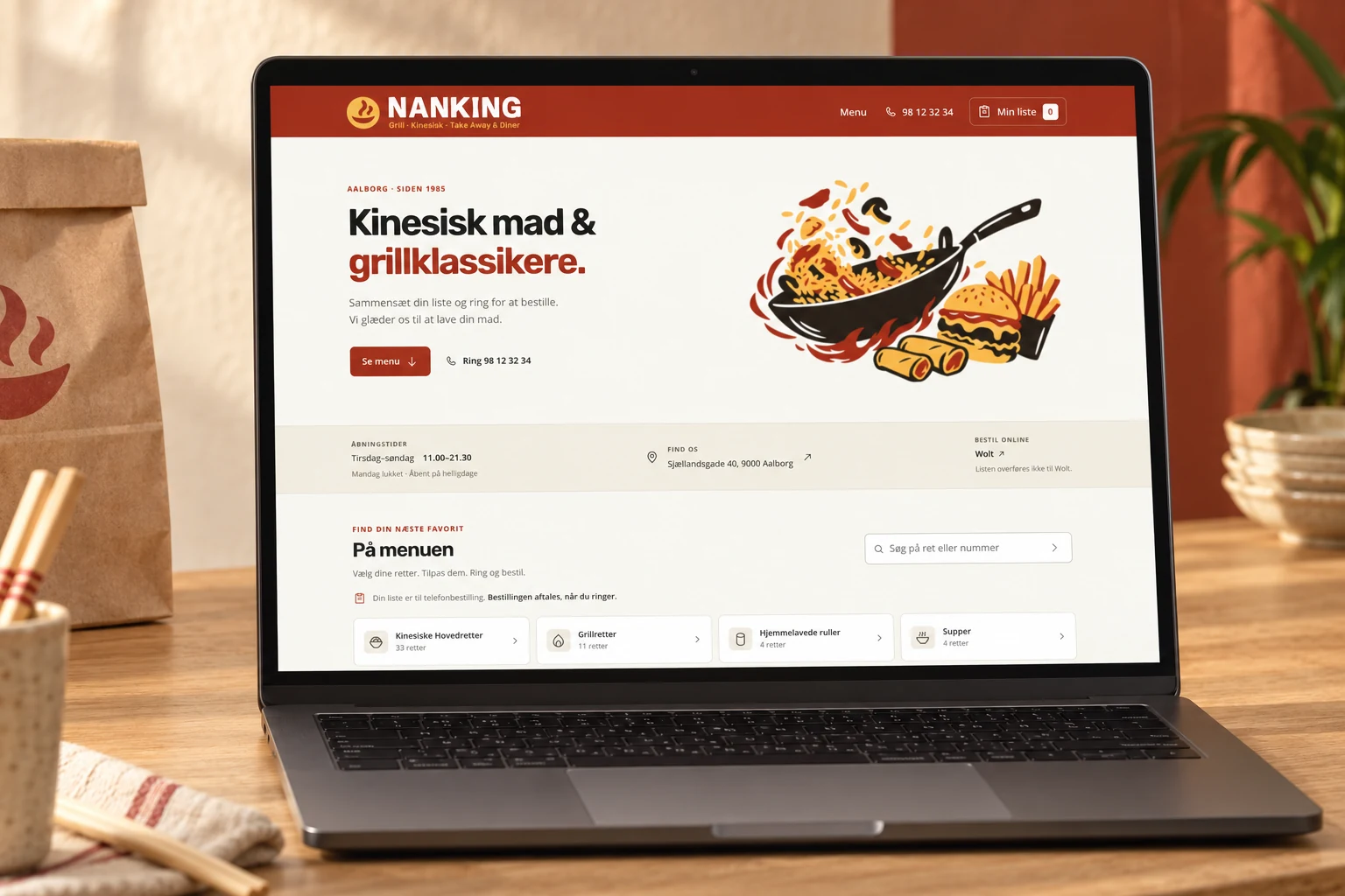 Nankings nye hjemmeside med logo på rød baggrund, cremefarver og wokillustration vist på en laptop i en restaurantmockup